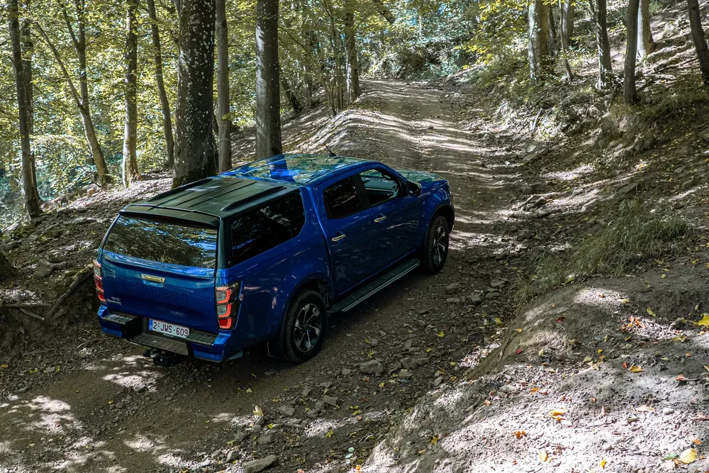 Pickup Isuzu bleu roulant sur un chemin forestier, sous une lumière naturelle.