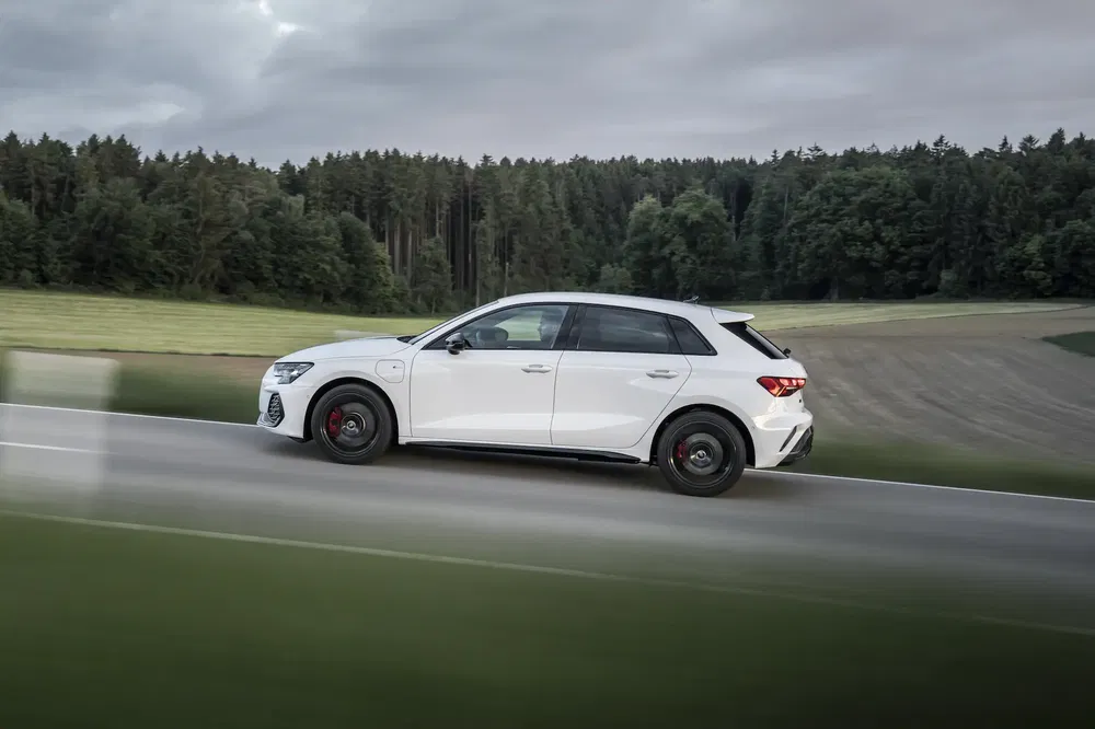 Audi A3 Sportback blanche sur route de campagne avec forêt en arrière-plan.