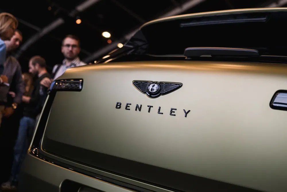 Logo Bentley sur le coffre arrière doré lors d'un salon automobile.