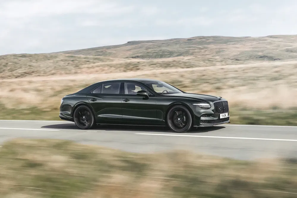 {"fr":"Bentley Flying Spur noire roulant sur une route de campagne panoramique.","nl":"Zwarte Bentley Flying Spur rijdt op een schilderachtige plattelandsweg."}