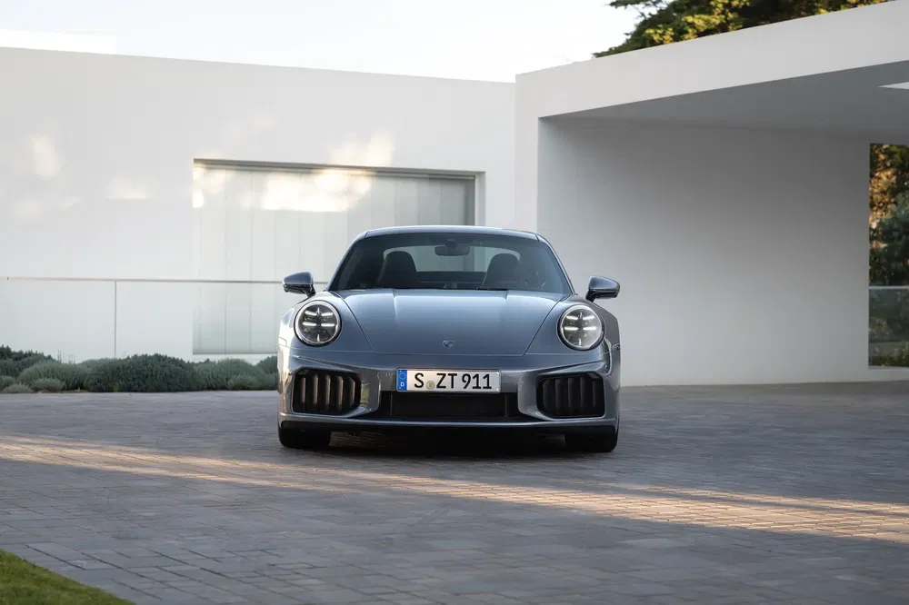 Porsche 911 grise garée devant une maison moderne, design élégant et classique.