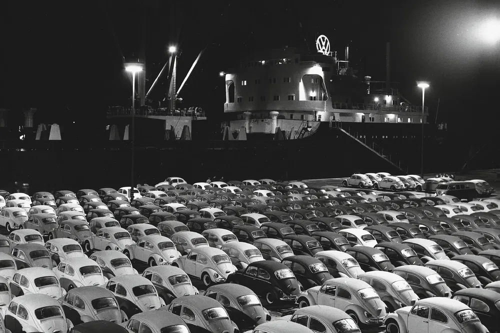 Vente de nuit de Volkswagen Beetle, nombreuses voitures alignées devant un cargo illuminé.