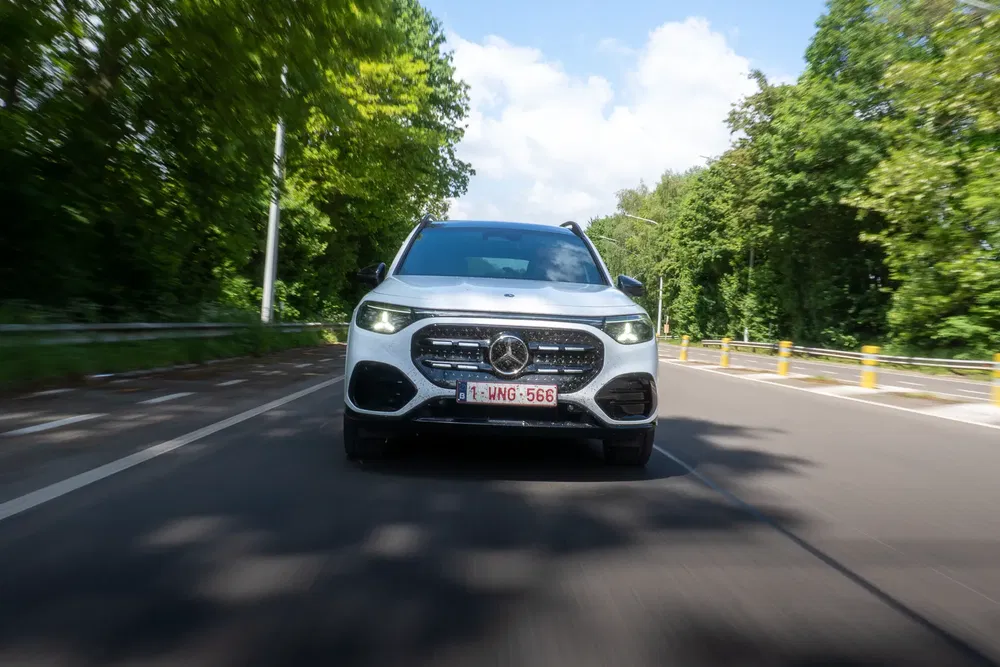 SUV Mercedes-Benz GLA blanc roulant sur une route bordée d'arbres, vue de face dynamique.