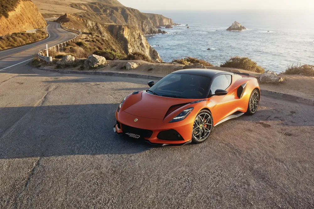 Lotus Emira orange sur une route côtière escarpée avec vue sur l'océan.