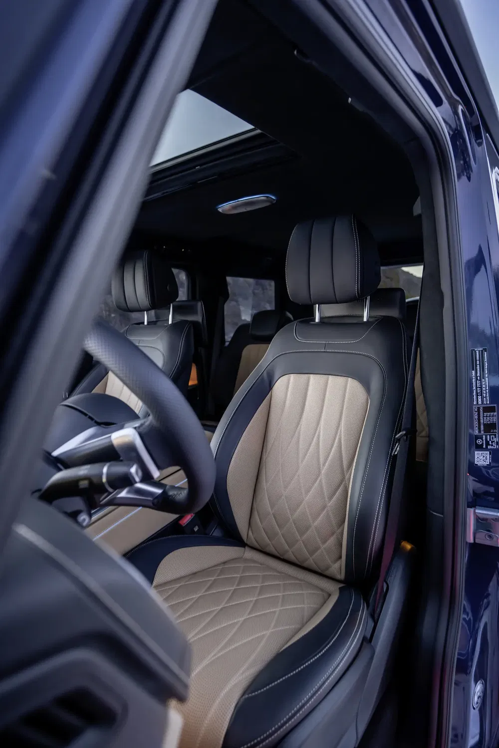 Luxe interieur van een Mercedes G-Klasse met beige leren stoelen en open dak.