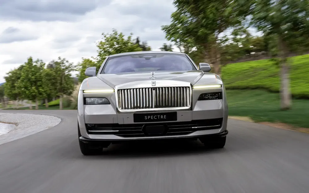 Rolls-Royce Spectre grise roulant sur une route bordée d'arbres.