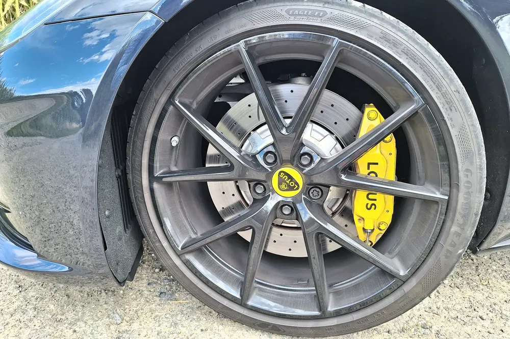 Lotus wiel met gele remklauwen en zwarte sportvelgen op een zanderige ondergrond.