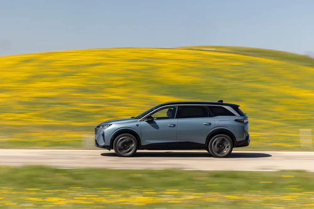 BMW iX SUV rijdt langs een weg met gele bloemenveld in de lente.
