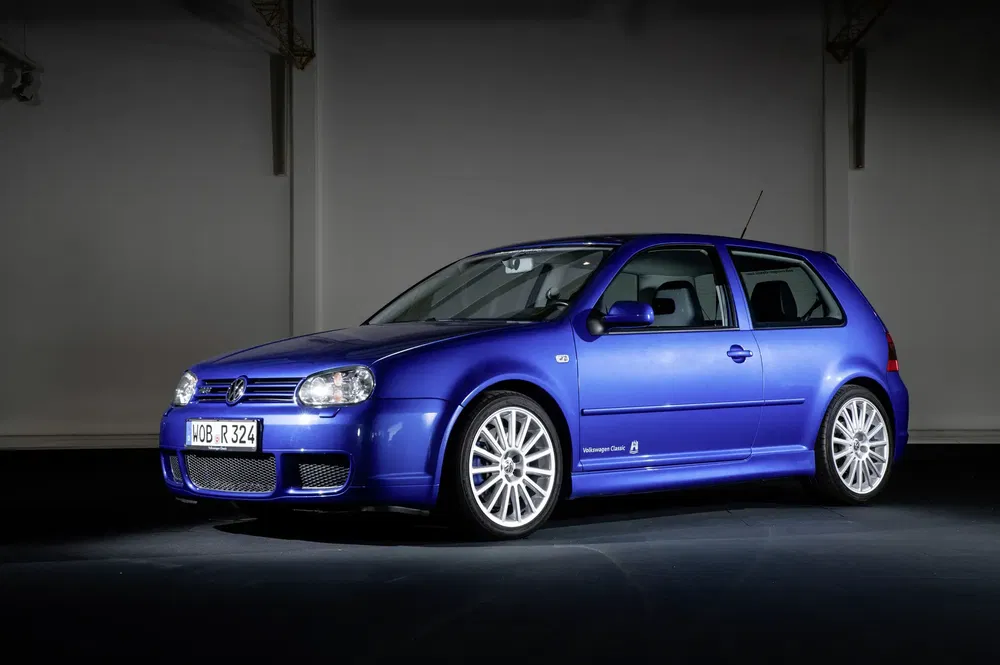 Blauwe Volkswagen Golf R32 geparkeerd in een donkere studio, glanzende zilveren velgen.