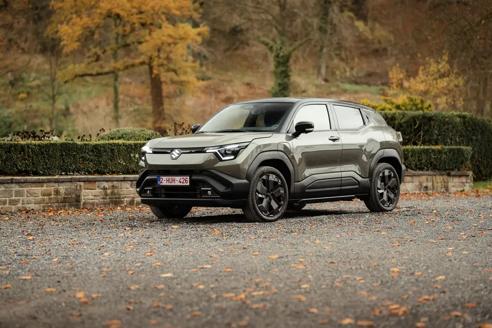 Compacte Suzuki SUV op een grindpad, omgeven door herfstlandschap en serene natuur.
