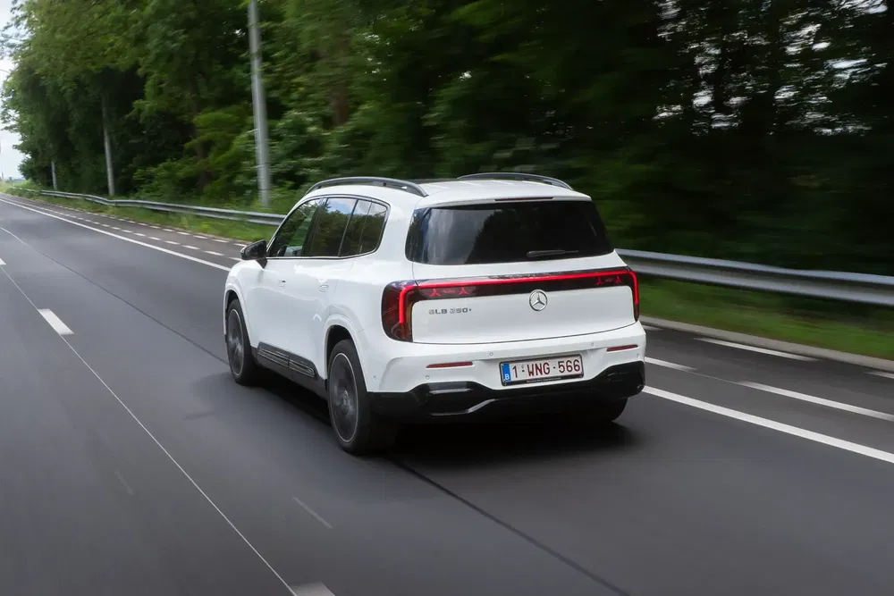 Mercedes-Benz EQB 350 blanc roulant sur une autoroute bordée d'arbres, vue arrière dynamique.