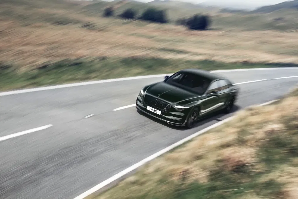 {"fr":"Voiture Bentley en mouvement rapide sur route de campagne sinueuse, paysage flou.","nl":"Bentley-auto snel rijdend op kronkelige plattelandsweg, vage achtergrond."}