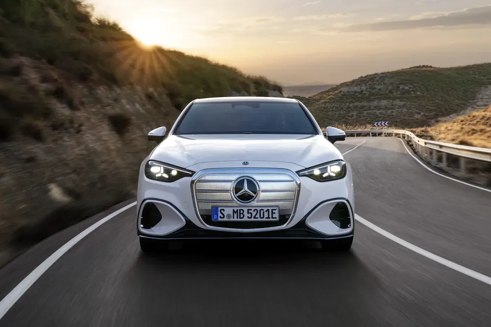 Mercedes-Benz EQE blanche sur route sinueuse au coucher du soleil, vue de face.