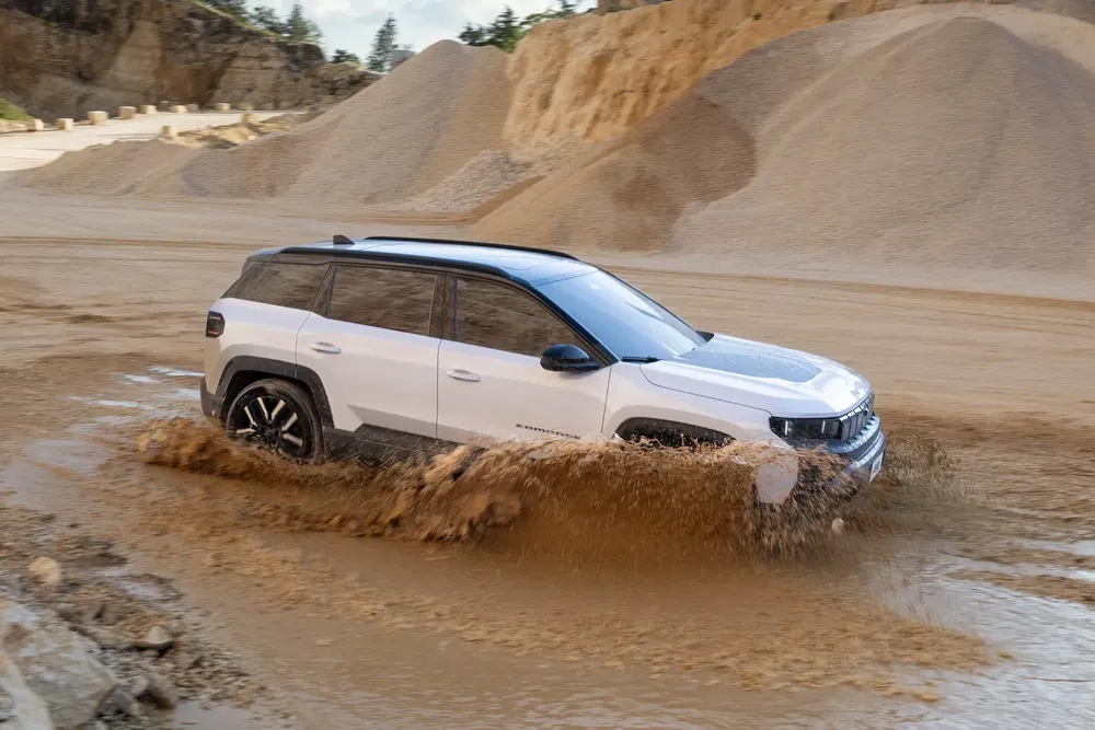 {"fr":"SUV Jeep blanc traverse une flaque de boue dans un paysage poussiéreux.","nl":"Witte Jeep SUV doorkruist modderplas in stoffig landschap."}
