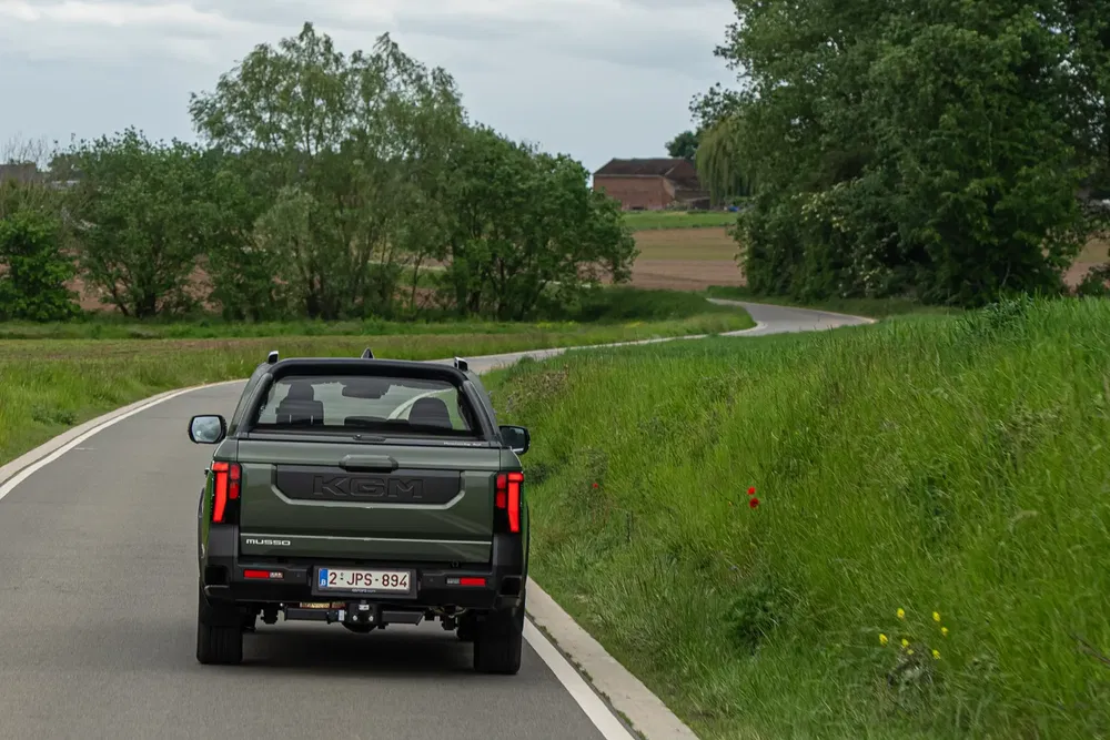 Pick-up Musso roulant sur une route de campagne sinueuse entourée de verdure.
