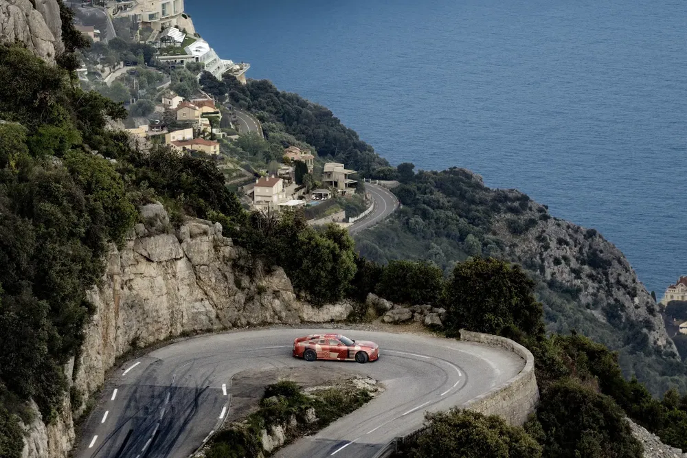 Voiture de sport rouge sur route sinueuse côtière, paysage pittoresque de bord de mer.