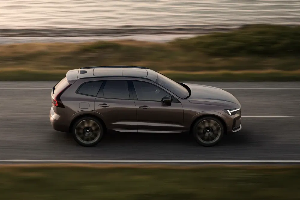 SUV Volvo XC60 gris roulant le long d'une route côtière, perspective latérale dynamique.