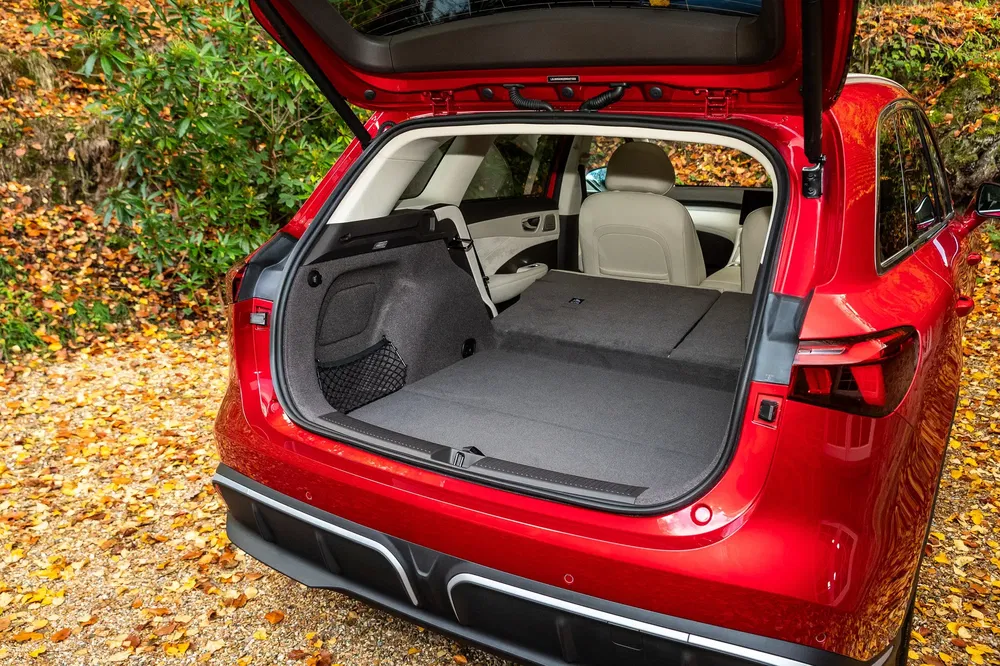 Ruime kofferbak van een rode SUV met neergeklapte stoelen, geparkeerd op herfstbladeren.