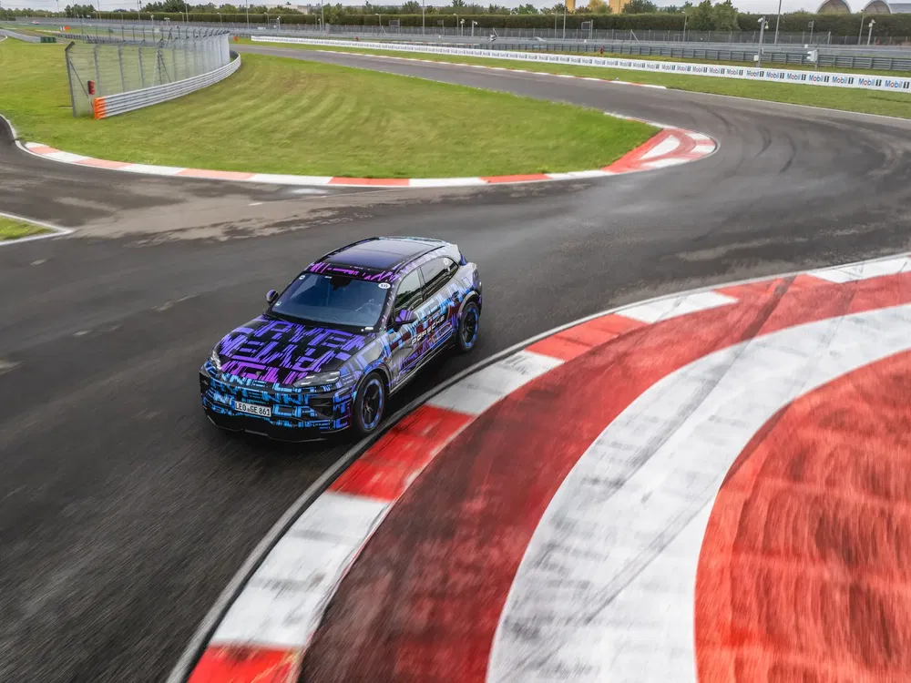 Gecombineerde SUV Audi Q6 E-Tron onder camouflage, scherpe bocht op racecircuit.