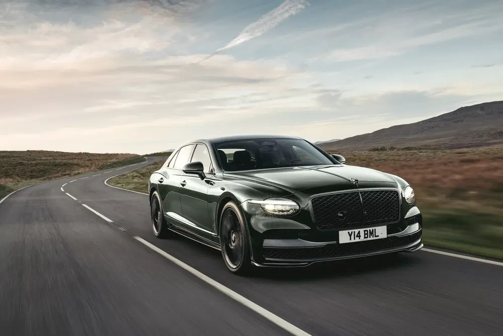 Berline Bentley Flying Spur verte roulant sur une route sinueuse, entourée de paysage montagneux.
