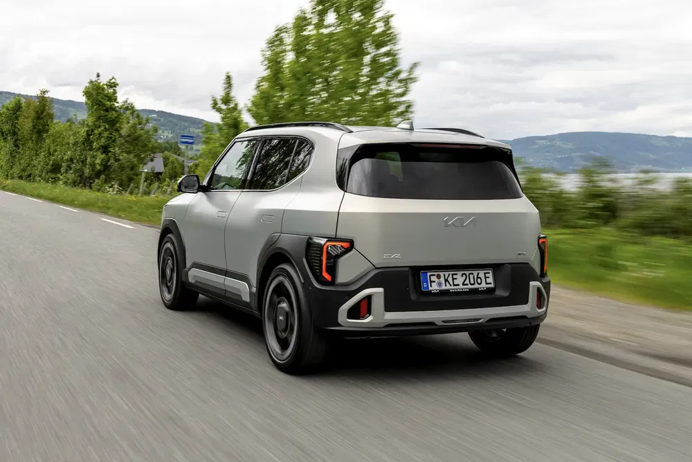Kia EV9 roulant sur une route rurale bordée d'arbres sous un ciel nuageux.
