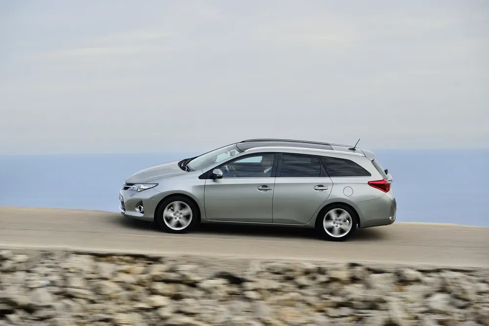 Grijze Toyota Auris Touring rijdt op een schilderachtige kustweg.