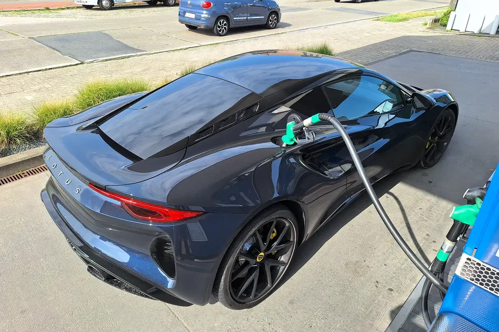 Zwarte Lotus Emira tankt bij tankstation, achteraanzicht.
