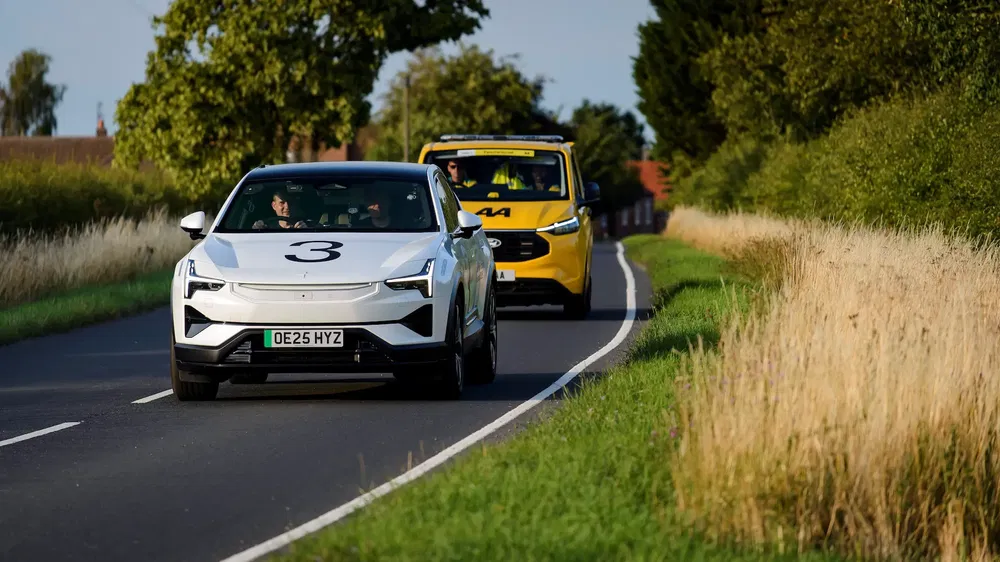 Voiture blanche Polestar 2 suivie par une camionnette jaune sur une route de campagne.