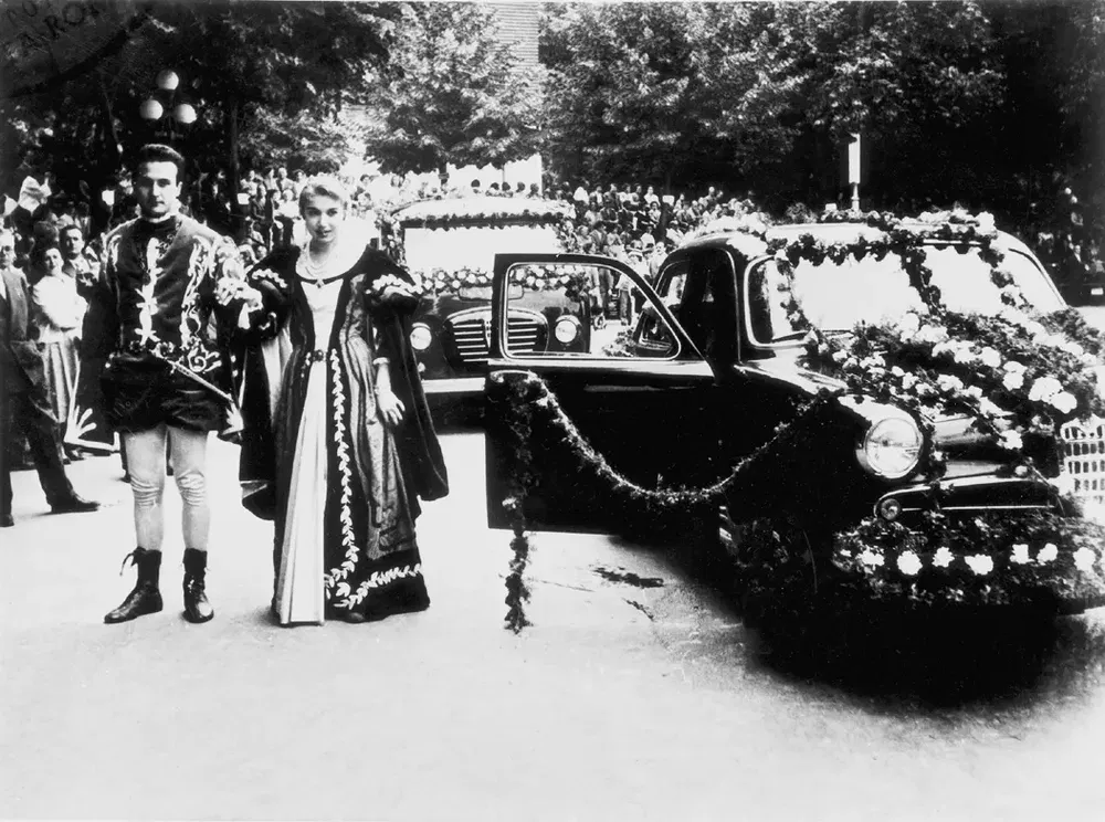 Une voiture décorée de fleurs avec des personnes en costumes d'époque lors d'un défilé.