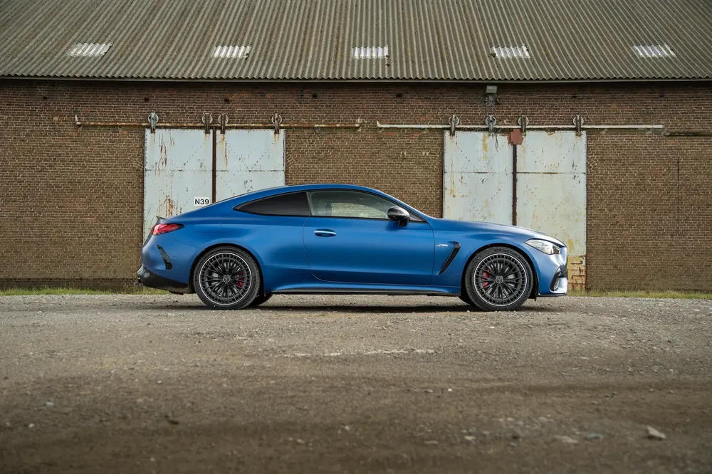 Mercedes-AMG Classe E coupé bleu devant un entrepôt industriel.