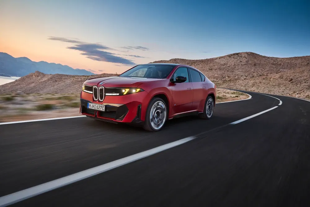 BMW électrique rouge sur une route sinueuse au crépuscule, paysage désertique en arrière-plan.
