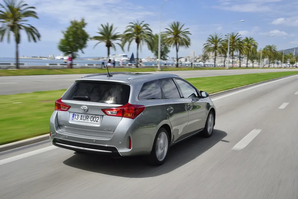 Grijze Toyota Auris rijdt op kustweg omgeven door palmbomen.
