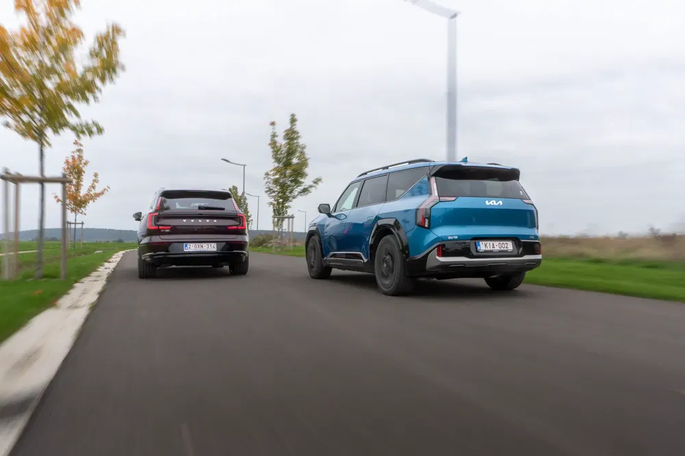 Deux SUV, un Kia bleu et un autre noir, roulant sur une route pavée.