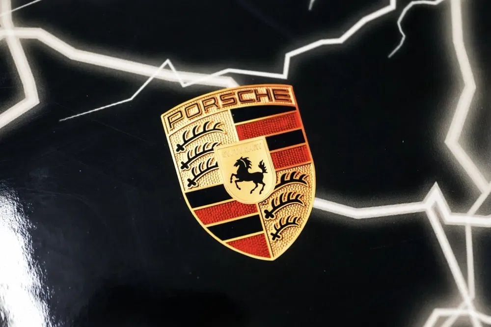 Porsche-embleem tegen zwarte achtergrond met opvallende witte bliksemontwerpen.