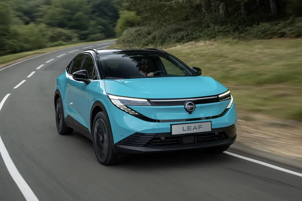 Nissan Leaf bleu vif roulant sur une route sinueuse bordée d'arbres verdoyants.