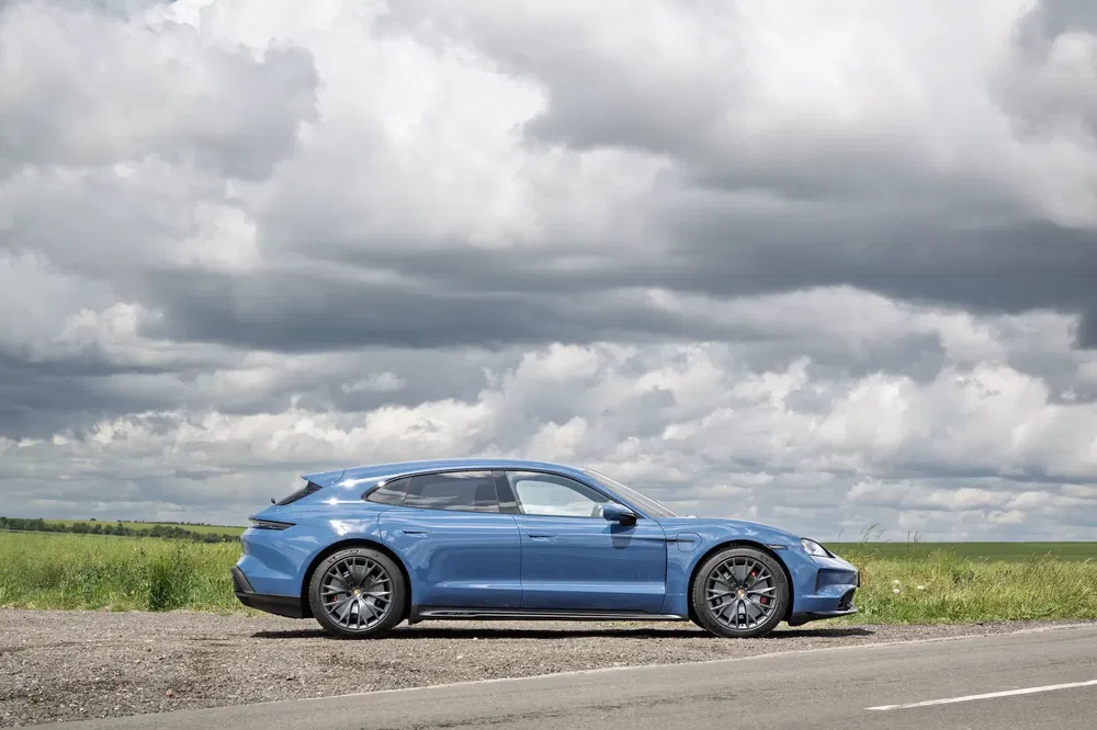 Porsche Taycan Cross Turismo bleu garé sous un ciel nuageux, sur une route de campagne.