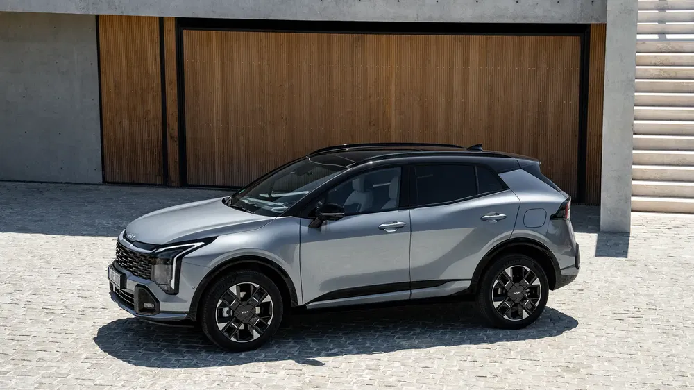 SUV Kia Sportage gris stationné sur des pavés devant un mur en bois moderne.