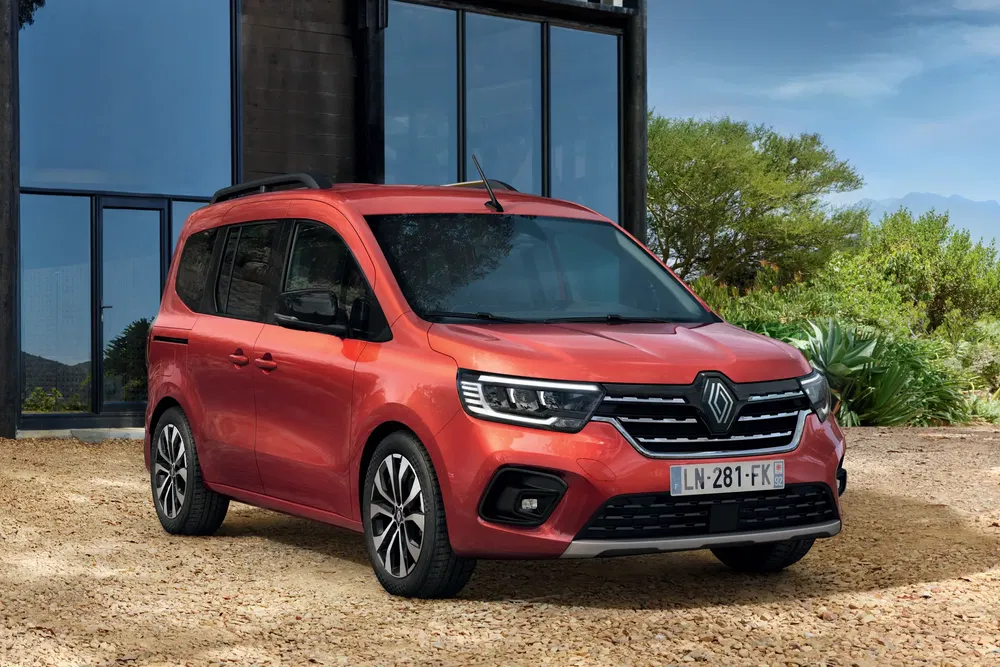 Rode Renault Kangoo geparkeerd voor een modern gebouw, elegante buitenkant.