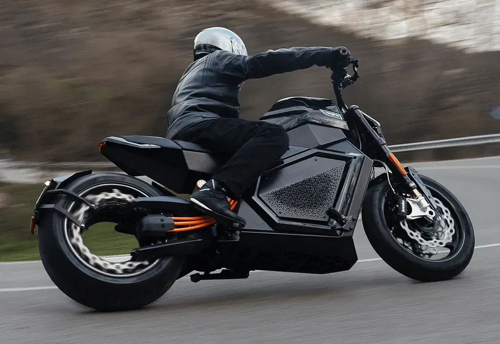 Motorrijder op futuristische elektrische motorfiets leunt in bocht op open weg.