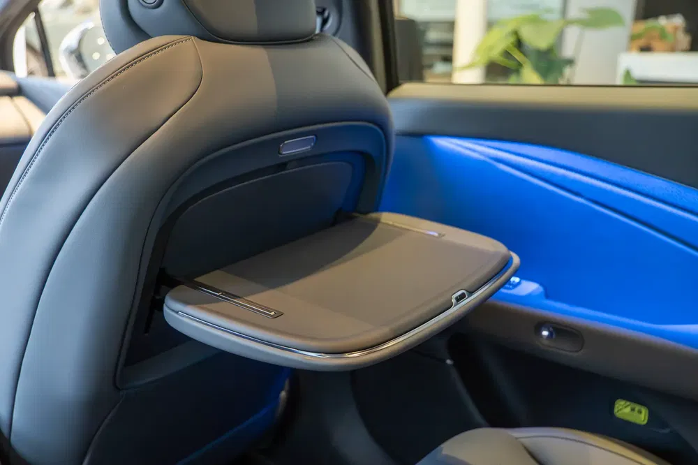 Opklapbaar tafeltje in moderne auto met stijlvol blauw interieur, geïntegreerd in achterstoel.