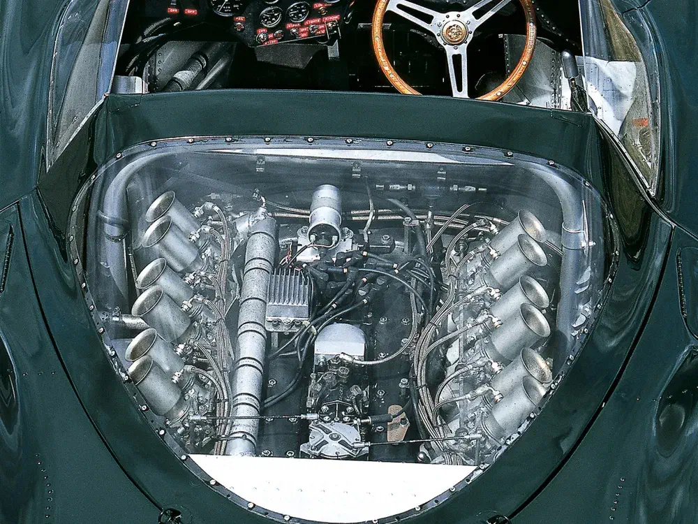 Vue détaillée du moteur V12 Jaguar Type E, tableau de bord et volant rétro en bois.