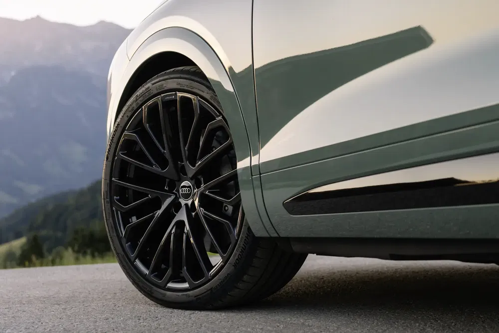 Roue en alliage noir d'une Audi sur route de montagne pittoresque au coucher du soleil.