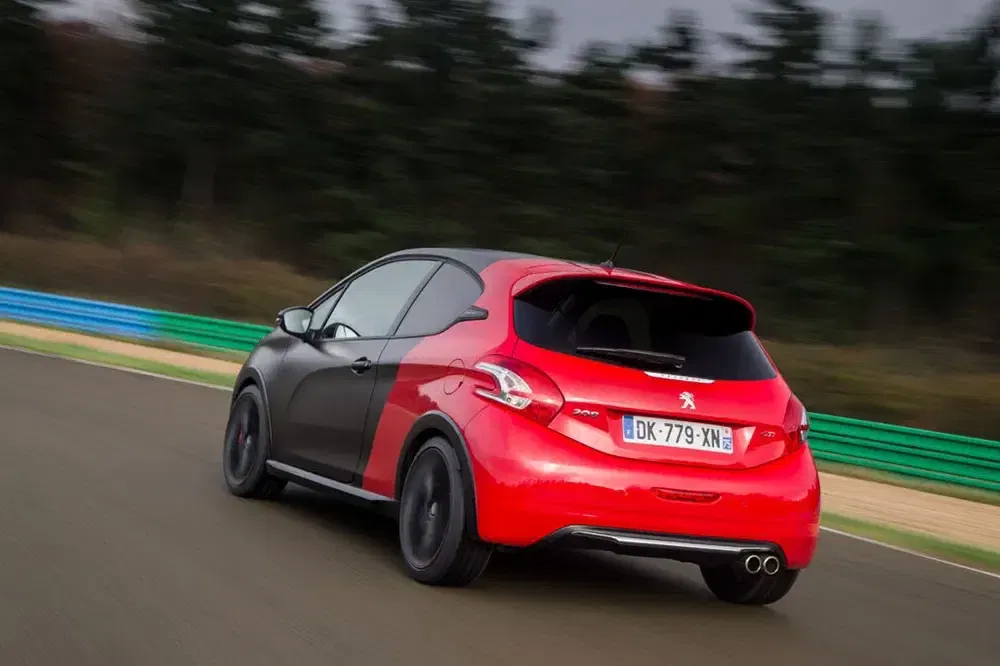 Peugeot 208 GTi bicolore rugissant sur circuit, arborant des nuances rouges et noires élégantes.
