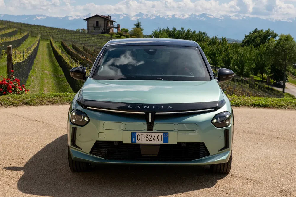 Groene Lancia auto geparkeerd voor glooiende wijngaarden, blauwe lucht op de achtergrond.