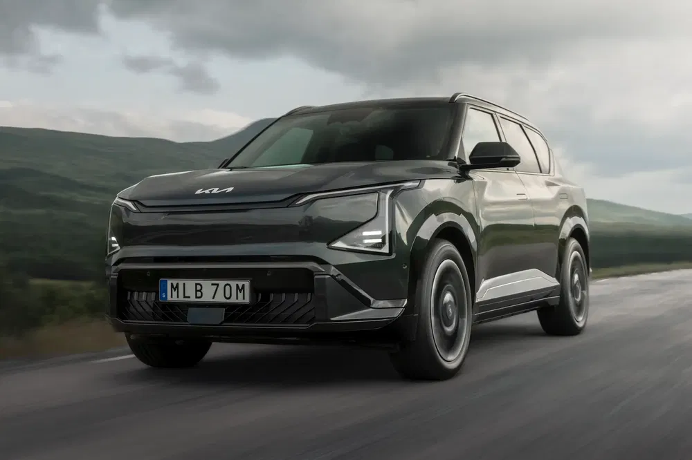 Moderne Kia SUV rijdt onder bewolkte hemel op open weg met bergen op achtergrond.