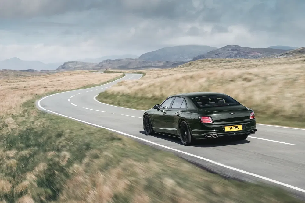 Bentley roulant sur une route sinueuse dans un paysage montagneux et champêtre.