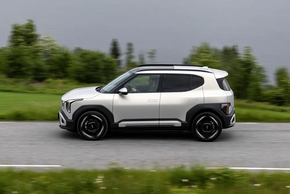 Kia EV5 électrique roulant sur route, paysage verdoyant en arrière-plan.