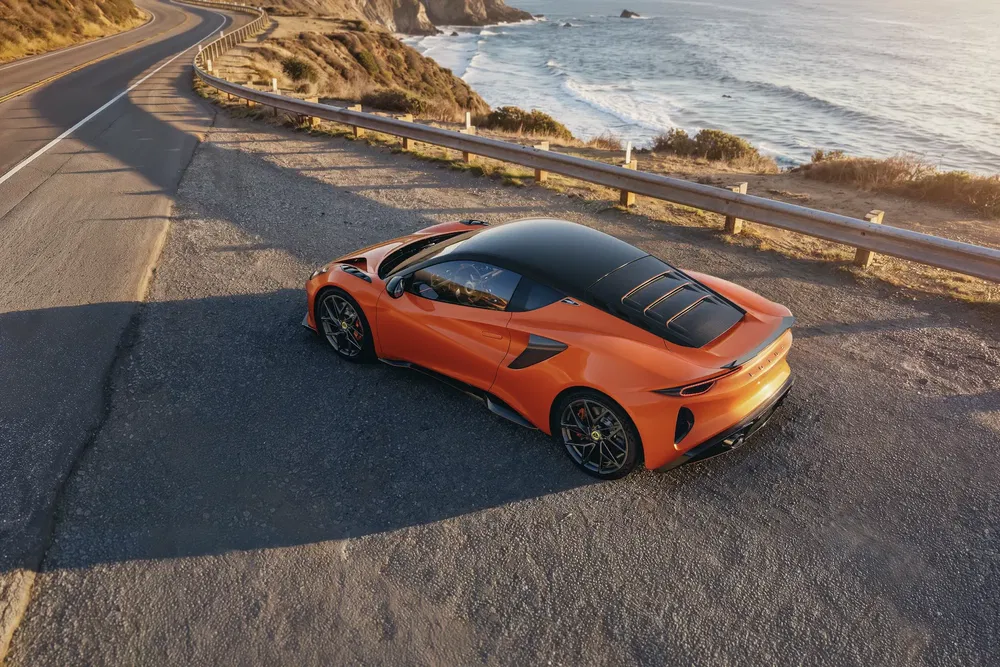 Voiture de sport Lotus sur une route côtière au coucher du soleil, vue arrière aérienne.