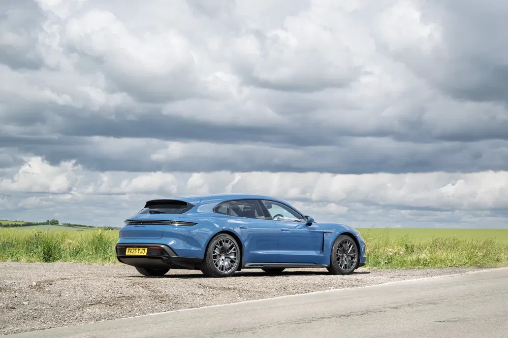 Porsche Taycan bleu sur une route de campagne sous un ciel nuageux.