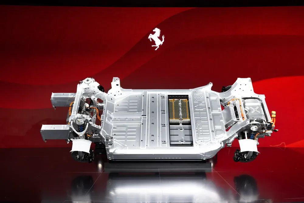 Châssis électrique Ferrari exposé sur fond rouge, montrant l'architecture de la batterie et des moteurs.